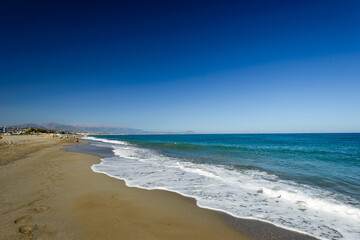 Fototapeta na wymiar Turquoise sea white foam yellow sand deep blue sky footprints in sand