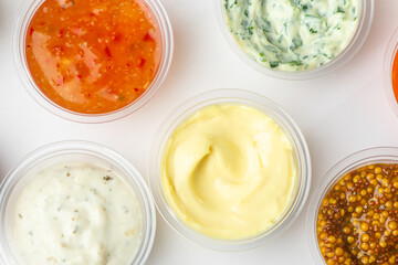 Top view on various sauces in small cups on white background