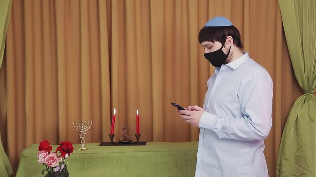 Before the chuppah ceremony, a Jewish groom in a protective mask in a synagogue hall dials an SMS by phone. Medium plan