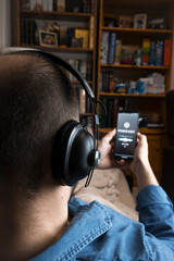 Closeup of a man lying on the couch at home with headphones listening to a podcast on his smartphone.
