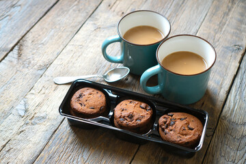 Two cups of coffee with milk and chocolate cookies stand on a rustic wooden table. Morning atmosphere.