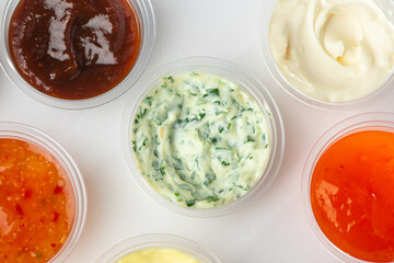 Top view on assortment of different sauces in small cups on white background