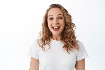 Fototapeta premium Close up of excited blond woman smiling pleased, looking with joy and gratitude, standing in t-shirt against white background
