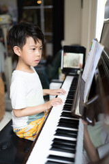 A boy is studying piano online with tablet.