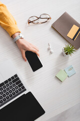 cropped view of woman holding smartphone with blank screen near laptop and credit card