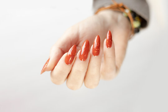 Woman hand with long nails and orange ginger and green manicure holds a bottle of nail polish