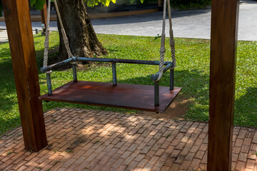 The swings hung below the brick floor. Children playground ayunan swing hanging in park garden. blank white wooden swing in flowers garden with nature background.