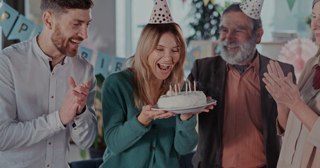 Excited caucasian blonde woman mother gathering her family around, holding cake and blowing candles...