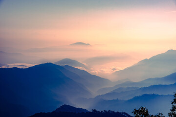 Fototapeta na wymiar View of Himalayas mountain range with visible silhouettes through the colorful fog at Binsar, a hill station in Almora district, Uttarakhand, India.
