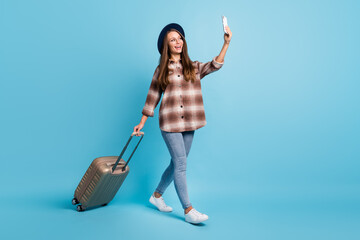 Full size profile side photo of young smiling girl go traveling with luggage take selfie on phone isolated on blue color background