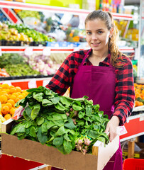 Young smiling woman salesman carrying box with fresh spinach at supermarket