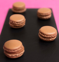 brown macarons with chocolate cream, on a black plate and a pink background