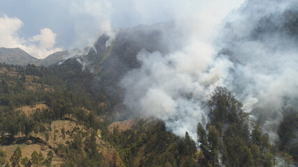 fire in mountain forest. aerial view forest fire and smoke on slopes hills. wild fire in mountains in tropical forest, Java Indonesia. natural disaster fire in Southeast Asia