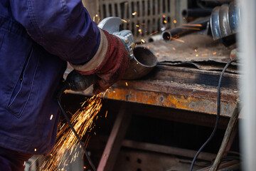 a man in working form is working on production, factory physical labor, a man is holding a Bulgarian, he is sawing an iron pipe with a metal disk, sparks are flying, dangerous work
