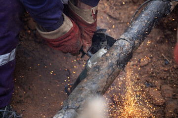 a man in working form is working on production, factory physical labor, a man is holding a Bulgarian, he is sawing an iron pipe with a metal disk, sparks are flying, dangerous work
