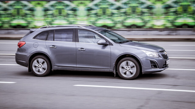 Chevrolet Cruze rides on a street. Gray 5-door station wagon motor car rushes on the road with blurred background