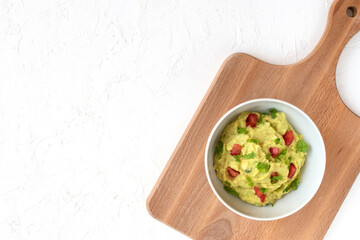 Fresh guacamole in a bowl on a kitchen board and white background