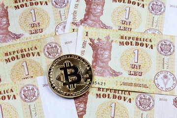 Close-up on a golden Bitcoin coin on top of a stack of Moldovan leu banknotes.