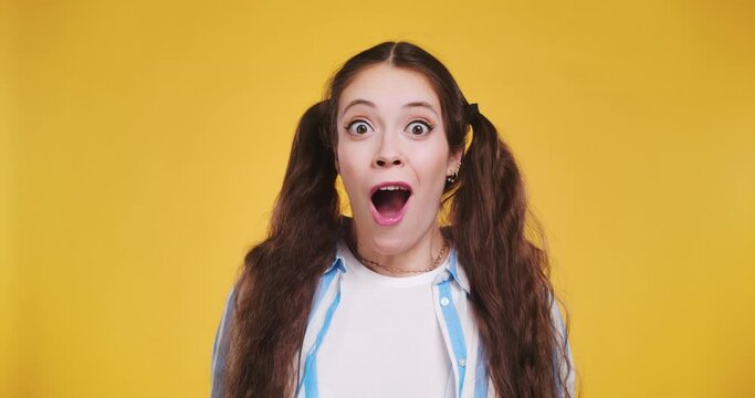 Happy fun charismatic young brunette woman posing isolated on yellow background. People wow emotion concept. Looking into a camera shocked and crazy surprised. Say wow slowly in slow motion.