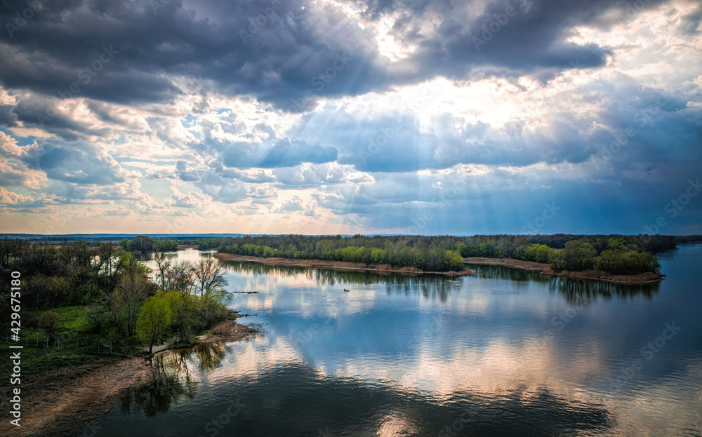 Wall mural Light of the setting sun through the clouds. River and sky	