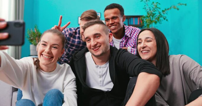 Joyous multi-ethnic group of friends sitting on couch together and taking selfie with smartphone while watching soccer match on TV