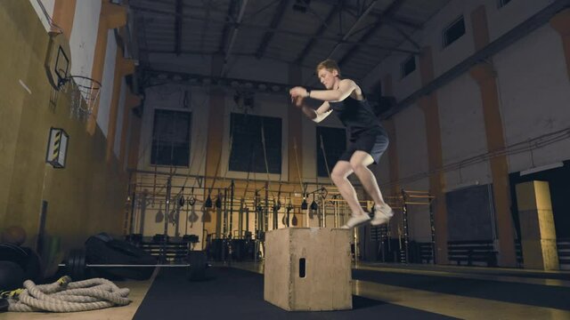 Young redhead man jumping on wooden box in gym