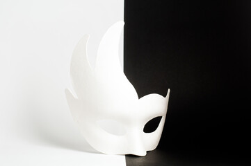 White carnival mask on a black and white background. The mask stands in the middle, between black and white. - obrazy, fototapety, plakaty
