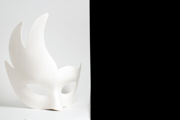 White carnival mask on a black and white background. The mask stands on a white background.