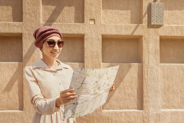 Happy woman travels alone and looks at a map against the wall of an ancient city in the Middle East region or somewhere in Morocco.