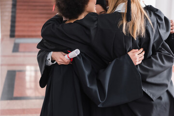 Cropped view of interracial graduates hugging in university