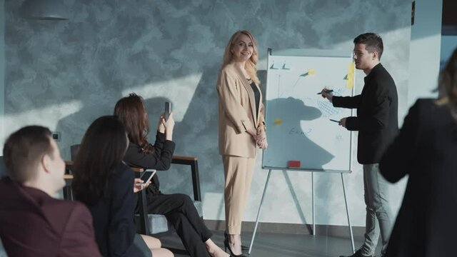 Group of business related coworkers wearing suits having teambuilding meeting and conference discussing company results. Girl in audience filming presentation and colleagues on phone.