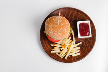 hamburger on a clay plate decorated with french fries and tomatoes on a white background.
