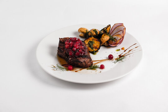 steak fillet mignon on a white plate decorated with cranberries and mushrooms champignons on a white background