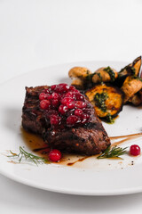 steak fillet mignon on a white plate decorated with cranberries and mushrooms champignons on a white background