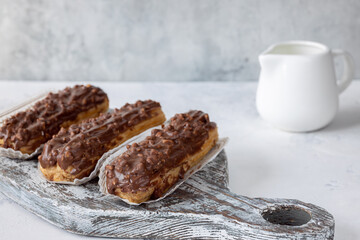 Three eclairs on the wooden grey board and creamer on grey background