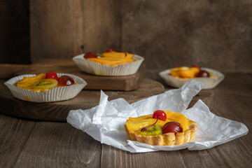 Four jelly tarts with fruits and cherry on white paper and on brown wooden background