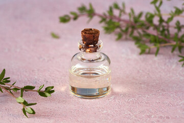 Essential oil bottle with fresh thyme twigs on a pastel pink background