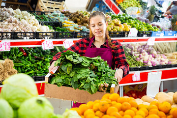 Cheerful european woman seller offering for sale fresh spinach at grocery store