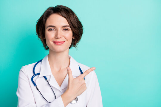 Photo of young woman doctor happy positive smile indicate finger empty space ad advice clinic isolated over teal color background