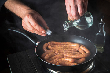The chef adds oil to pan with raw meat sausage. Preparation for cooking sausages in the kitchen of a restaurant or cafe