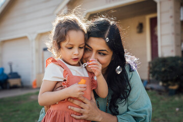 Obraz premium Mom hugging daughter blowing bubbles in front yard