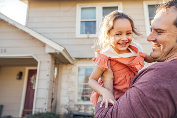 Dad holding happy smiling daughter in front of home