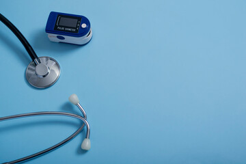 Fototapeta na wymiar Flat composition with pulse oximeter and stethoscope on blue background.A pulse oximeter used to measure heart rate and oxygen levels.