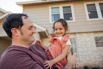 Dad holding happy smiling daughter in front of home