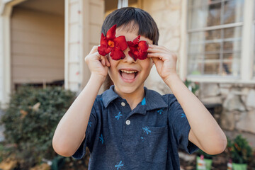 Smiling boy holding red flowers in front of eyes