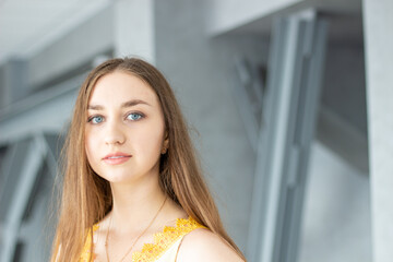 portrait of a beautiful young long blond hair and blue eyes woman in yellow blouse with building walls and posts background