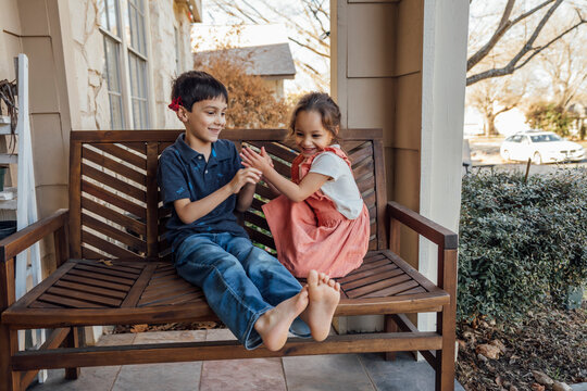 Boy And Girl Sitting On Front Porch Bench Playing Together