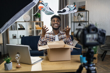 Cheerful afro man in headset creating video content for his social networks while unpacking new...