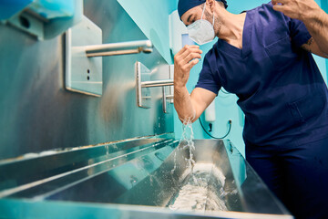 young Caucasian surgeon in scrubs washes his hands before entering the operating room in hospital
