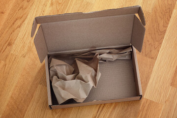 Open cardboard box with crumpled paper inside on a wooden background